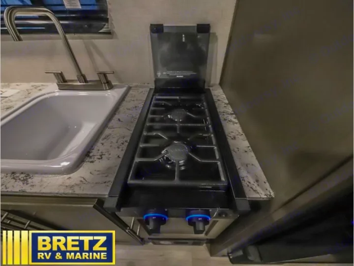 This RV rental kitchenette features a compact sink with a modern faucet and a two-burner gas stove for cooking on the go.. K-Z RV Sportsmen Classic 2024