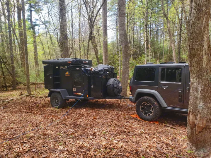 Jeep towing an off-road camping trailer in a forest. Ideal for your next RV rental wilderness adventure!. Off Grid Trailers Off Grid Trailers Trailer 2021