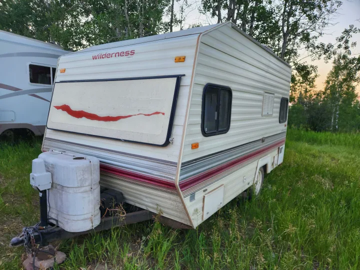 This white Wilderness travel trailer, with red & grey stripes, is parked in a grassy field. Perfect for an rv rental.. Fleetwood Wilderness 1991