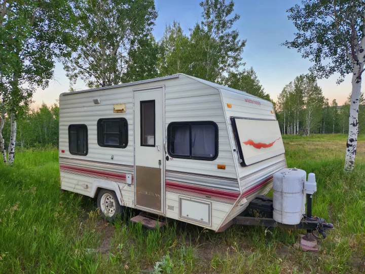 This cozy Wilderness travel trailer, perfect for an RV rental, sits in a grassy field with trees.. Fleetwood Wilderness 1991