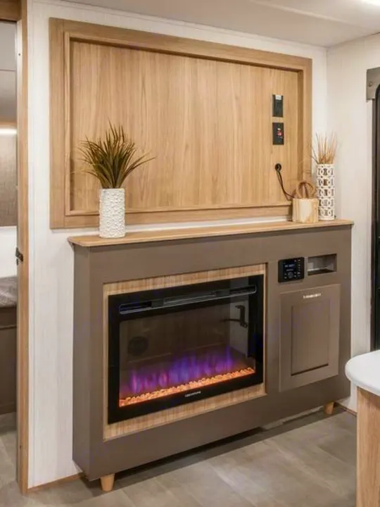 RV rental living area with a modern entertainment unit, decorative wood panel, and electric fireplace with purple flames.. Cruiser RV Avenir 2024