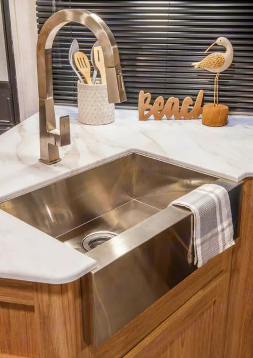 Modern kitchen sink in an RV rental, featuring a stainless steel farmhouse sink, stylish faucet, and decor.. Cruiser RV Avenir 2024