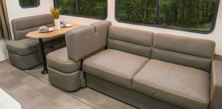 Spacious RV rental interior with comfortable gray dining booth and sofa seating, overlooking a forest view.. Cruiser RV Avenir 2024