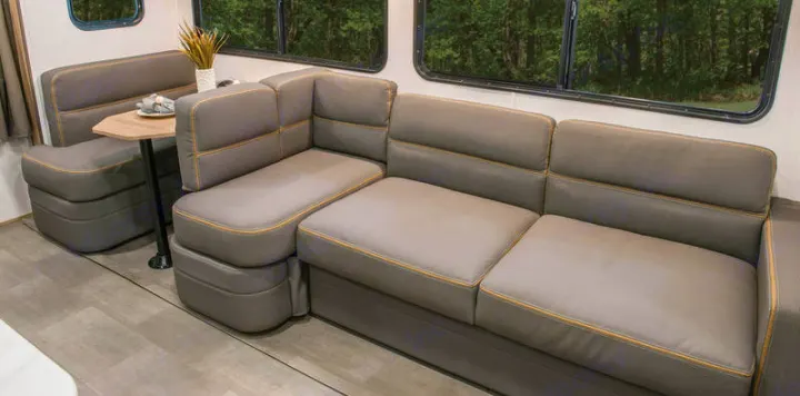 A modern gray U-shaped sectional sofa and dinette with a small table inside a spacious RV rental.. Cruiser RV Avenir 2024
