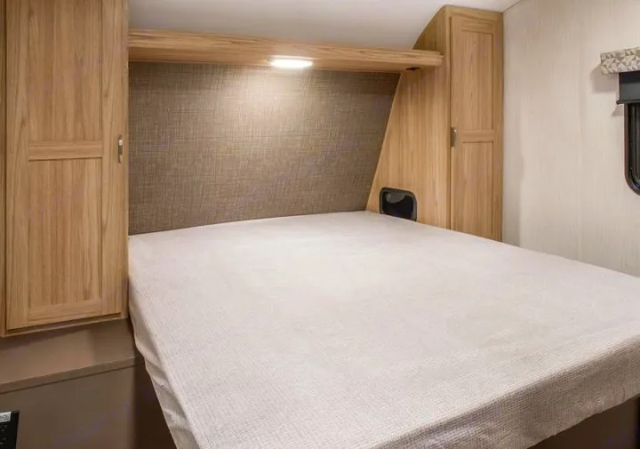 Interior of an RV rental bedroom featuring a full bed, overhead light, and integrated wood cabinets for efficient space.. Cruiser RV Avenir 2024