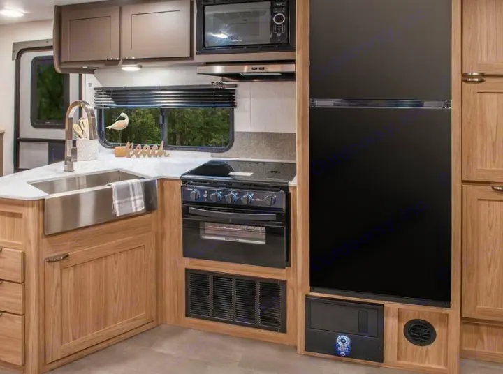 Fully equipped RV rental kitchen: stainless sink, stove, microwave, and refrigerator in light wood cabinets.. Cruiser RV Avenir 2024