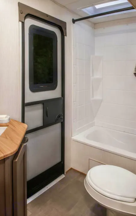 Spacious RV rental bathroom featuring a shower-tub combo, toilet, and an interior door with a window for your comfort.. Cruiser RV Avenir 2024