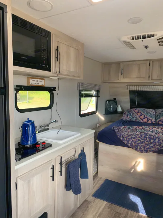 RV rental interior featuring a practical kitchen with a microwave, sink, and stovetop, alongside a comfortable bedroom.. KZ Sportsmen classic 160QB 2021