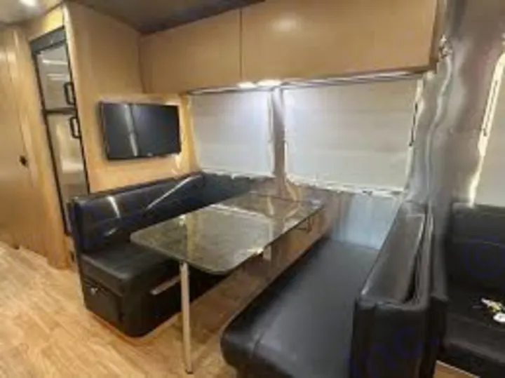 Spacious RV rental interior featuring a modern dinette with black booth seating, table, windows, TV, and fridge. Ideal for travel.. Airstream Flying Cloud 2016