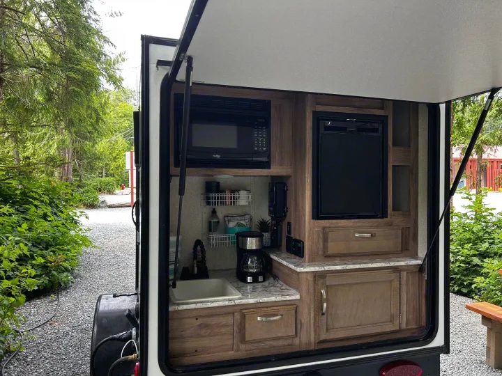 This RV rental offers an equipped outdoor mobile kitchen with microwave, fridge, and sink, set in a natural, green environment.. Jayco Hummingbird 2019