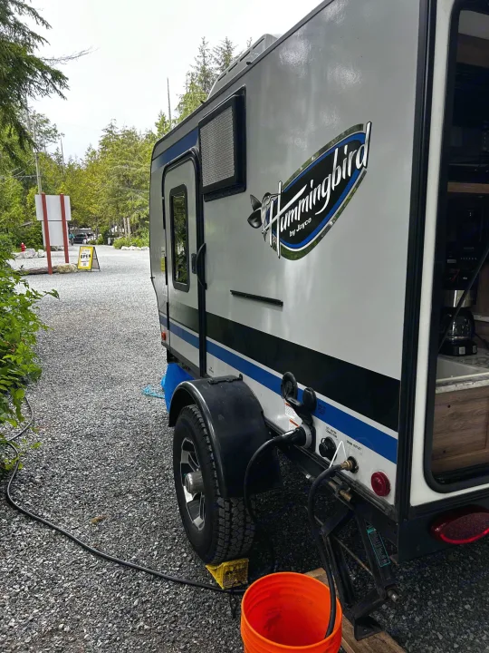 A Hummingbird by Jayco RV rental is parked on gravel at a campsite, with power/water hookups. Trees visible.. Jayco Hummingbird 2019