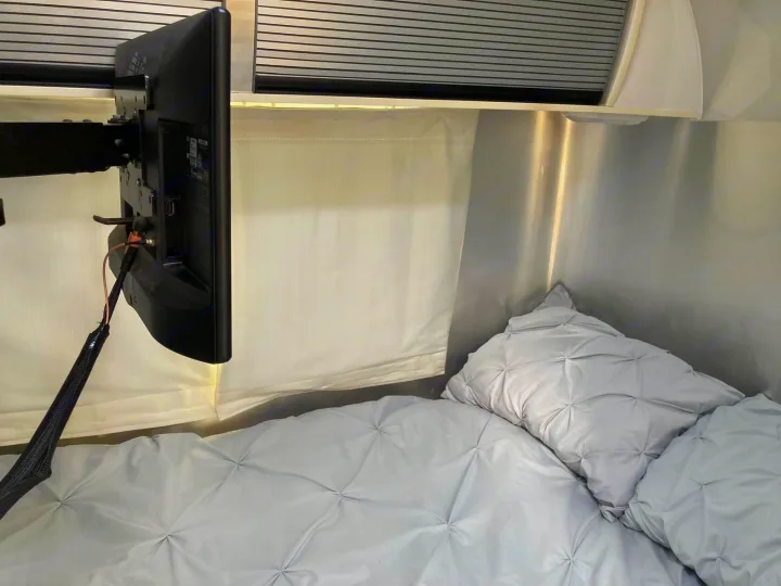 Cozy RV rental bedroom with a mounted TV, soft grey quilted bedding, and metallic walls. Ideal for comfortable travel.. Airstream Sport 2017