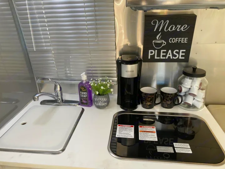 This RV rental features a compact kitchenette with a sink, coffee maker, mugs, pods & "More Coffee Please" sign. Ideal for trips!. Airstream Sport 2017