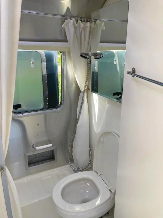Bright RV rental bathroom with a compact shower, toilet, window, and towel bar.. Airstream Sport 2017