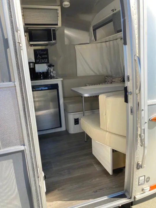 Step inside this inviting RV rental: a compact kitchen with microwave, coffee bar, and fridge, plus comfy dinette seating.. Airstream Sport 2017