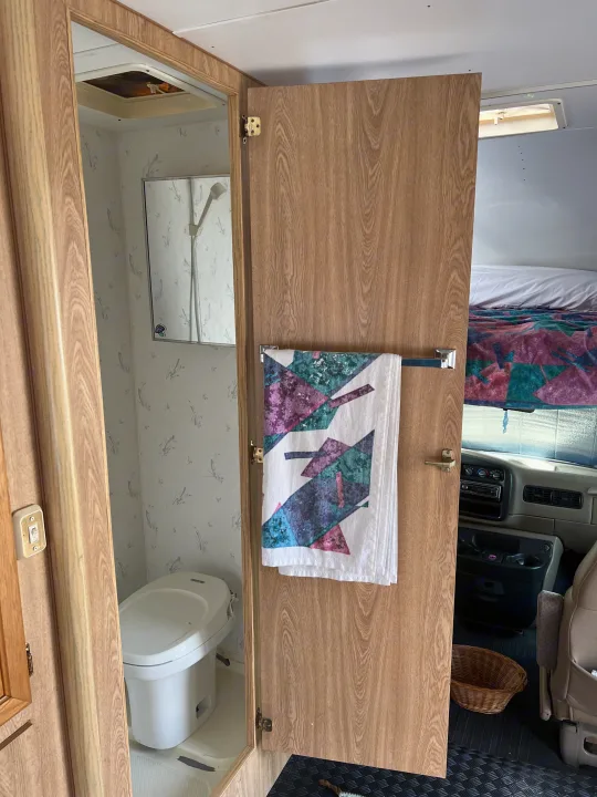 RV rental interior: A compact bathroom with toilet and shower is visible, with a colorful towel on the door leading to the front cabin.. Chevrolet Slumber Queen 1997