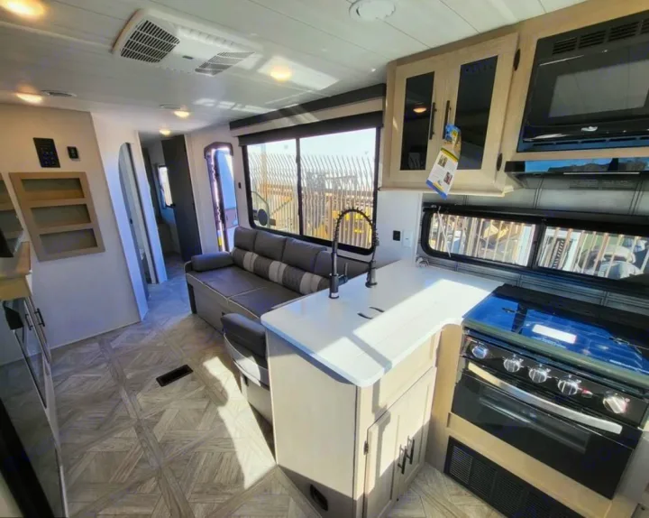 Bright RV rental interior: modern kitchen with stove, microwave, and sink, plus a comfy living area sofa.. Forest River Wildwood X-Lite 2024