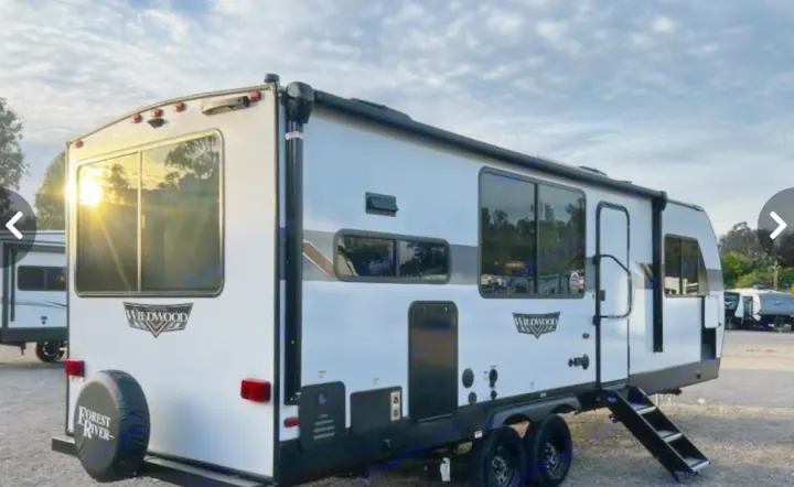 Modern Wildwood travel trailer for RV rental. This white camper features a rear spare tire and large windows.. Forest River Wildwood X-Lite 2024