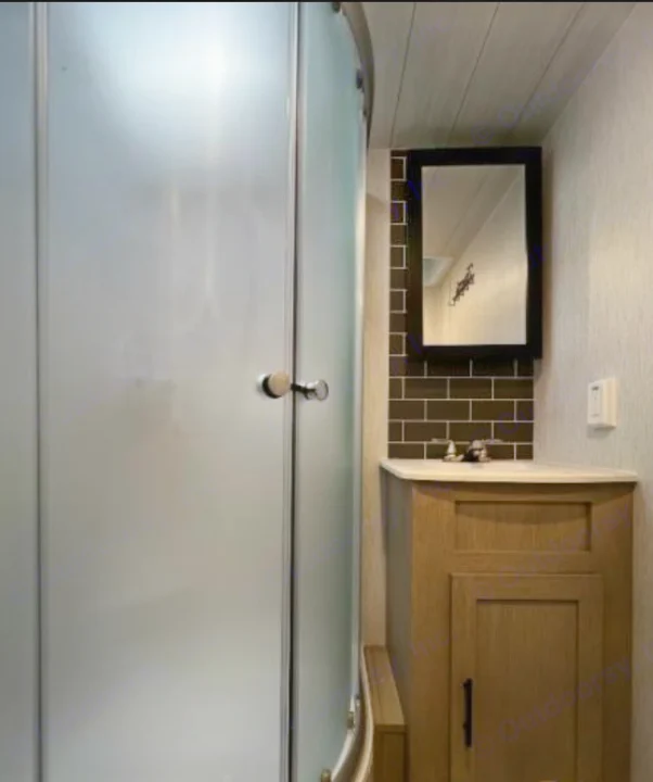 This compact RV rental bathroom features a frosted glass shower and wood vanity with sink and mirror.. Forest River Wildwood X-Lite 2024