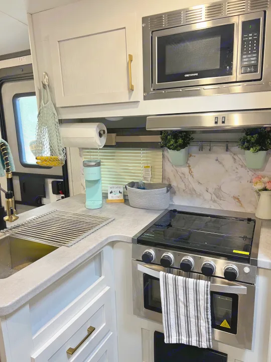 Bright RV rental kitchen featuring a microwave, stovetop, sink, and light teal Keurig, ready for cooking and coffee.. Keystone RV Astoria 2903BH 2022