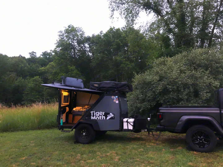 This compact 'Tiger Moth' camping trailer rv rental, pulled by a pickup truck, is set up in a lush, green outdoor spot.. TAXA TAXA Trailer 2019