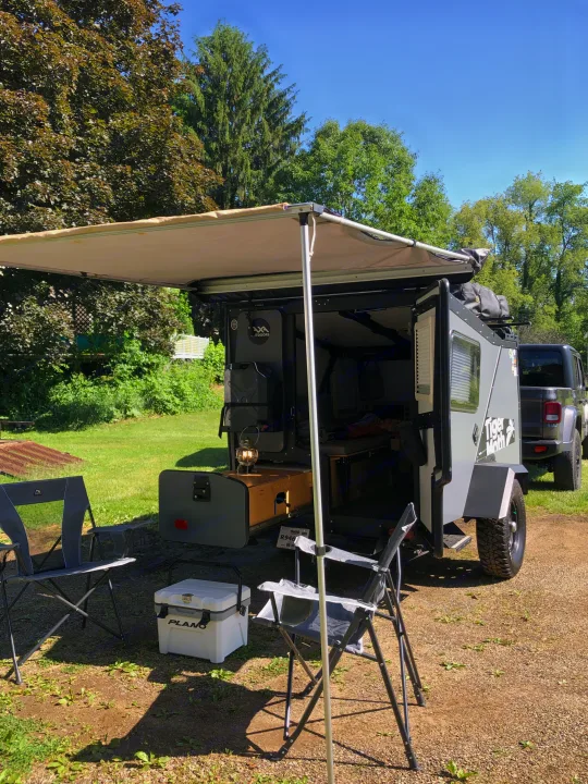 This compact Tiger Moth off-road camper, ideal for RV rental adventures, features an awning, chairs, and kitchen setup.. TAXA TAXA Trailer 2019