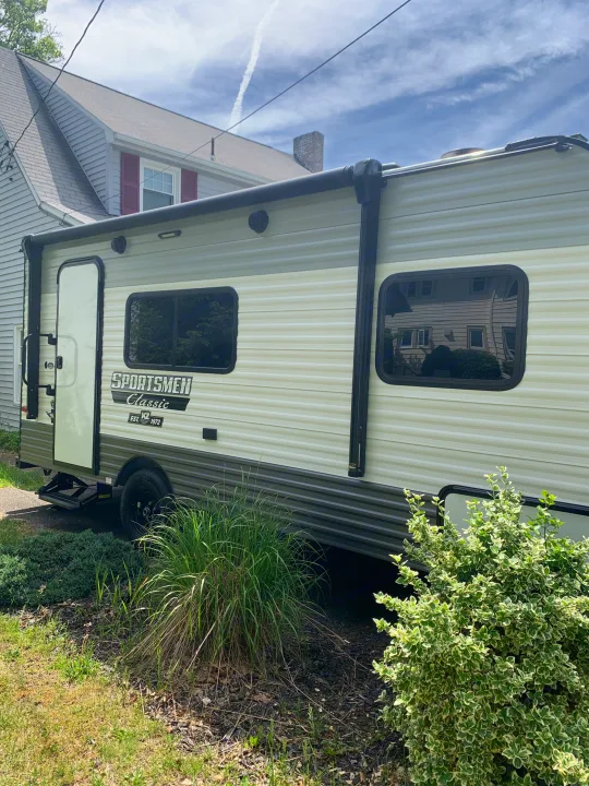 Side view of a light-colored Sportsmen Classic travel trailer, an RV rental, parked outdoors on a sunny day.. KZ Sportsmen classic 160QB 2021
