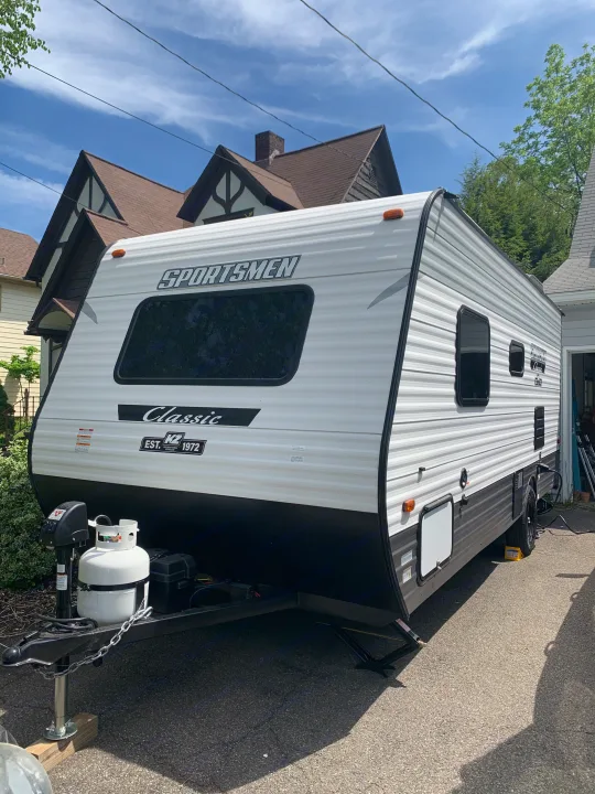 A white Sportsmen Classic travel trailer, ideal for an RV rental, is parked on a driveway under a clear sky.. KZ Sportsmen classic 160QB 2021