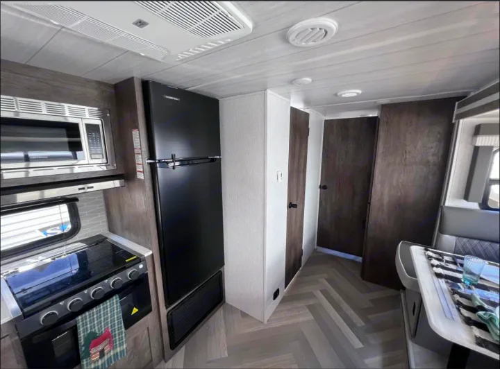 View of a modern RV rental interior, showing the kitchen area with a microwave, stove, refrigerator, and dining nook.. Forest River Salem Cruise Lite 2022