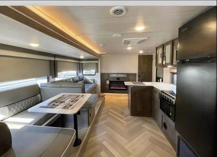Inside a modern RV rental: spacious kitchen, dining booth, and living area with fireplace, featuring sleek finishes.. Forest River Salem Cruise Lite 2022
