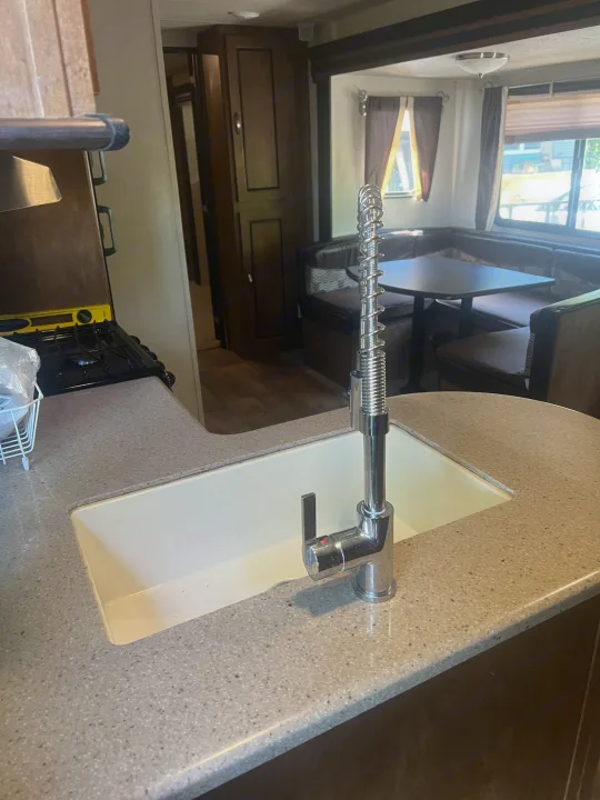 Inside this RV rental: A modern kitchen with a pull-down faucet and a U-shaped dining booth, ideal for comfort on the road.. Forest River Wildwood 2018