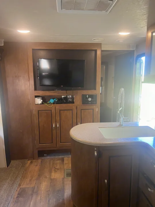 Inside an RV rental: a cozy living area with TV, entertainment center, and a kitchen island with a sink.. Forest River Wildwood 2018