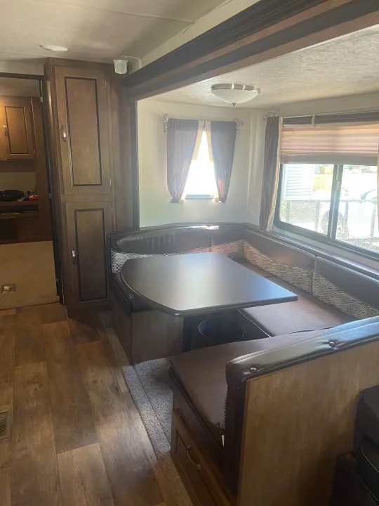 Interior of an RV rental: a comfortable dinette with U-shaped booth, table, wood flooring, and windows.. Forest River Wildwood 2018