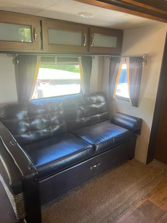 Spacious RV rental interior featuring a dark leather sofa, overhead storage cabinets, and bright side windows.. Forest River Wildwood 2018