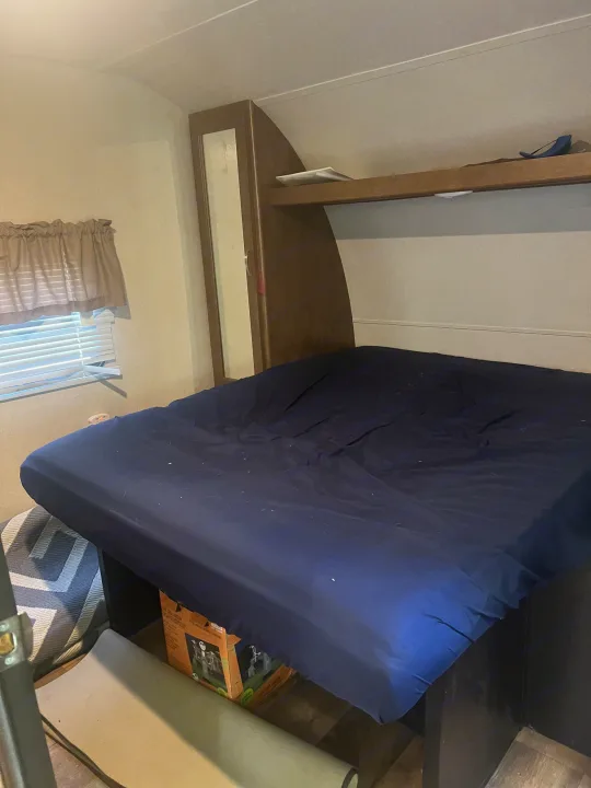 RV rental interior: compact bedroom featuring a navy blue bed, window, and integrated storage.. Forest River Wildwood 2018