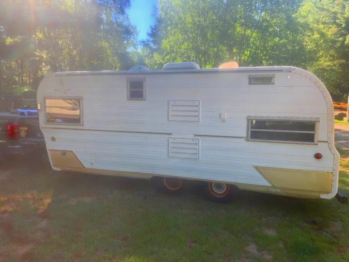 Classic white & gold travel trailer for RV rental, parked on grass in a treed outdoor setting.. Glendale Golden Falcon 1967