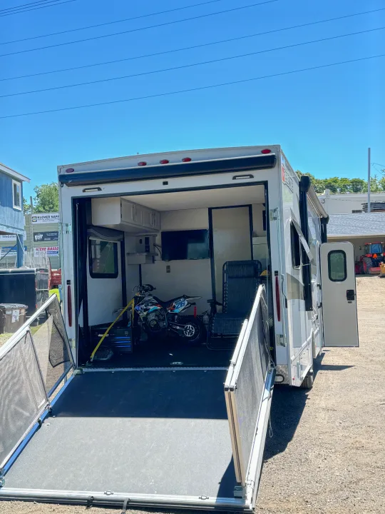 Explore with this RV rental toy hauler, featuring a dirt bike and living space accessible via its large rear ramp.. Thor Outlaw 2024