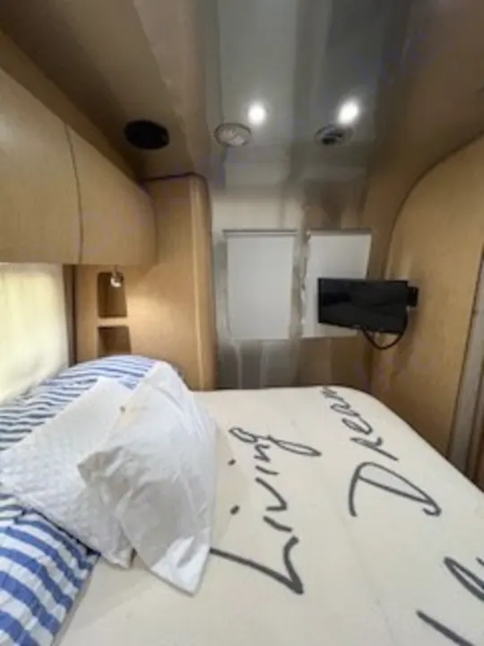 Experience comfort in this **RV rental** bedroom, featuring a comfy bed, mounted TV, and sleek interior for your travel adventures.. Airstream Flying Cloud 2016