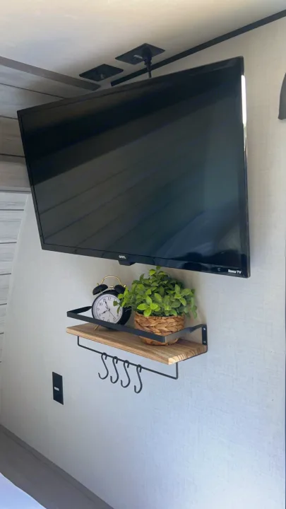 RV rental: Compact wall-mounted TV setup with shelf, alarm clock, plant, and hooks in an RV interior.. Coleman Lantern 17B 2024
