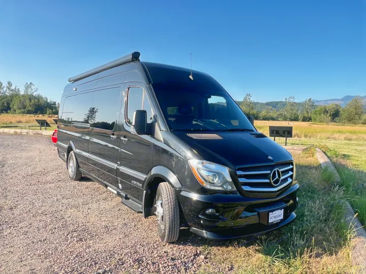 Black Airstream Mercedes Sprinter RV rental parked on gravel in a scenic outdoor park with mountains and trees.. Airstream Interstate 2016