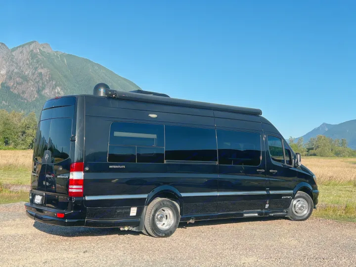 Sleek black Airstream Interstate RV rental, a Mercedes Sprinter camper van, ready for adventures by scenic mountains.. Airstream Interstate 2016