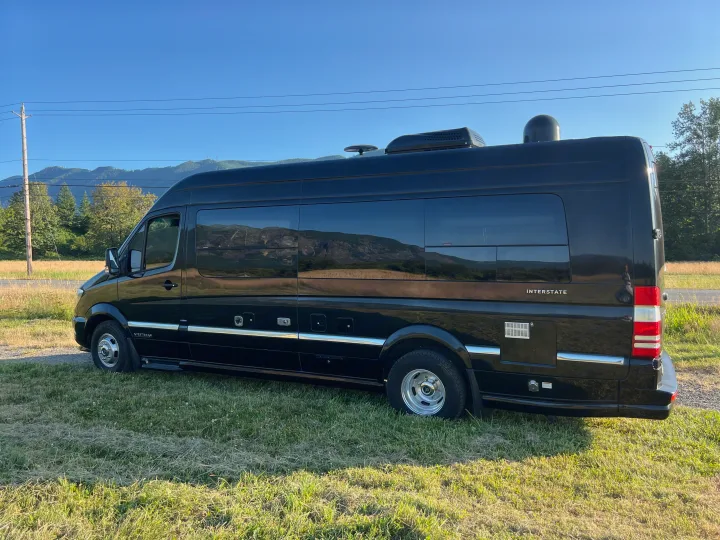 Spacious black Airstream Interstate RV rental van, perfect for road trips, parked outdoors with scenic mountain views.. Airstream Interstate 2016
