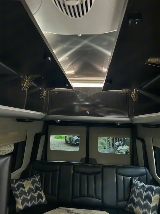 Spacious RV rental interior: plush black leather seating, overhead storage, and a bright, reflective ceiling.. Airstream Interstate 2016