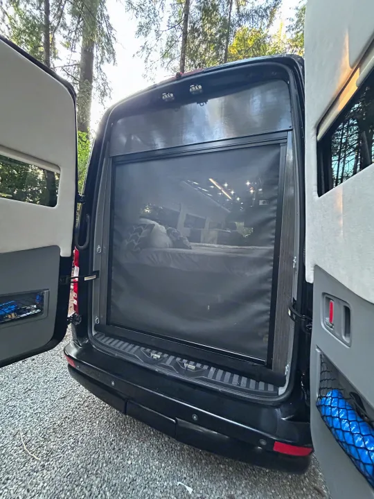 Open back doors of an RV rental revealing a comfortable bed with a mosquito screen, perfect for peaceful camping nights.. Airstream Interstate 2016