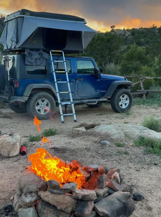 Blue Jeep with rooftop tent and cozy campfire at sunset. An adventurous **rv rental** alternative for outdoor camping!. Jeep Wrangler 2010