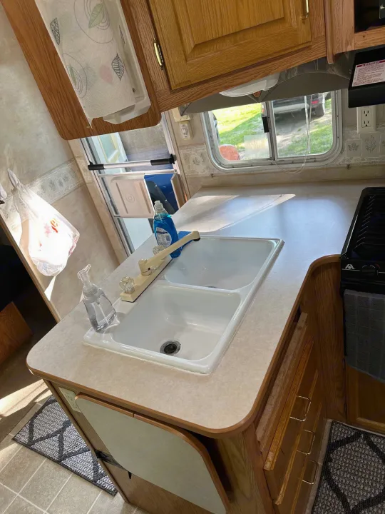 Clean RV rental kitchen with a double sink, counter, stove, and window view.. Jayco Jay Flight 2003