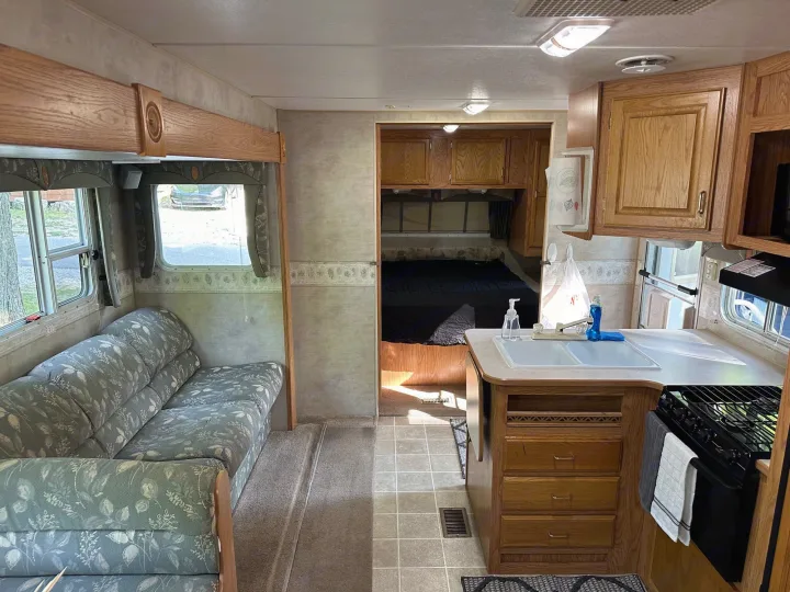 Spacious rv rental interior showing living area, kitchen, and bedroom. Features wood cabinets & floral sofa.. Jayco Jay Flight 2003