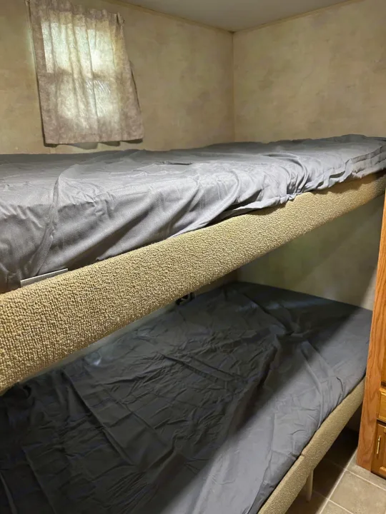 Cozy RV rental bunk beds with gray sheets and a window, ideal for extra sleeping space on your trip.. Jayco Jay Flight 2003