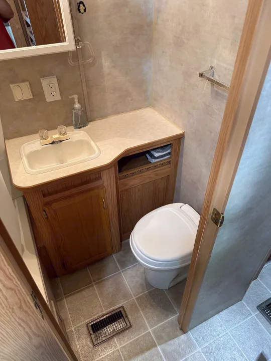 Compact RV rental bathroom features a sink, mirror, toilet, and wood cabinetry, ideal for travel trailer adventures.. Jayco Jay Flight 2003