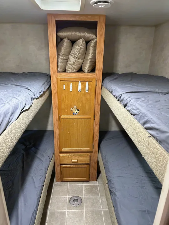 RV rental bunk beds and central storage unit, ideal for family travel. Features tidy grey bedding & wood accents.. Jayco Jay Flight 2003